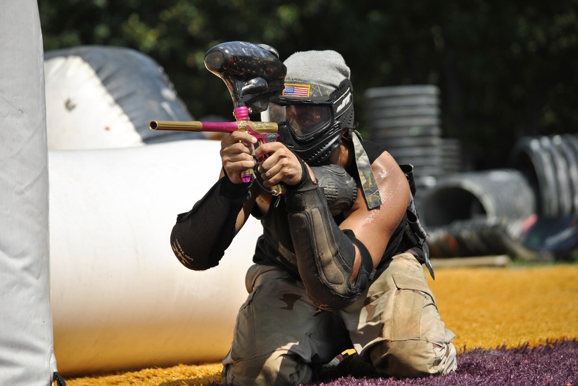 Player wearing protective paintball pants aiming a paintball marker on an outdoor field